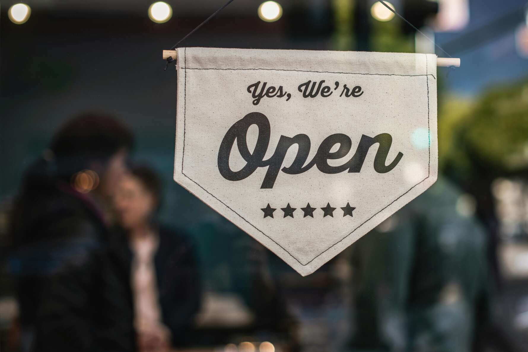 Photo of a sign saying "Yes, we're open" hanging at the door of a small business.