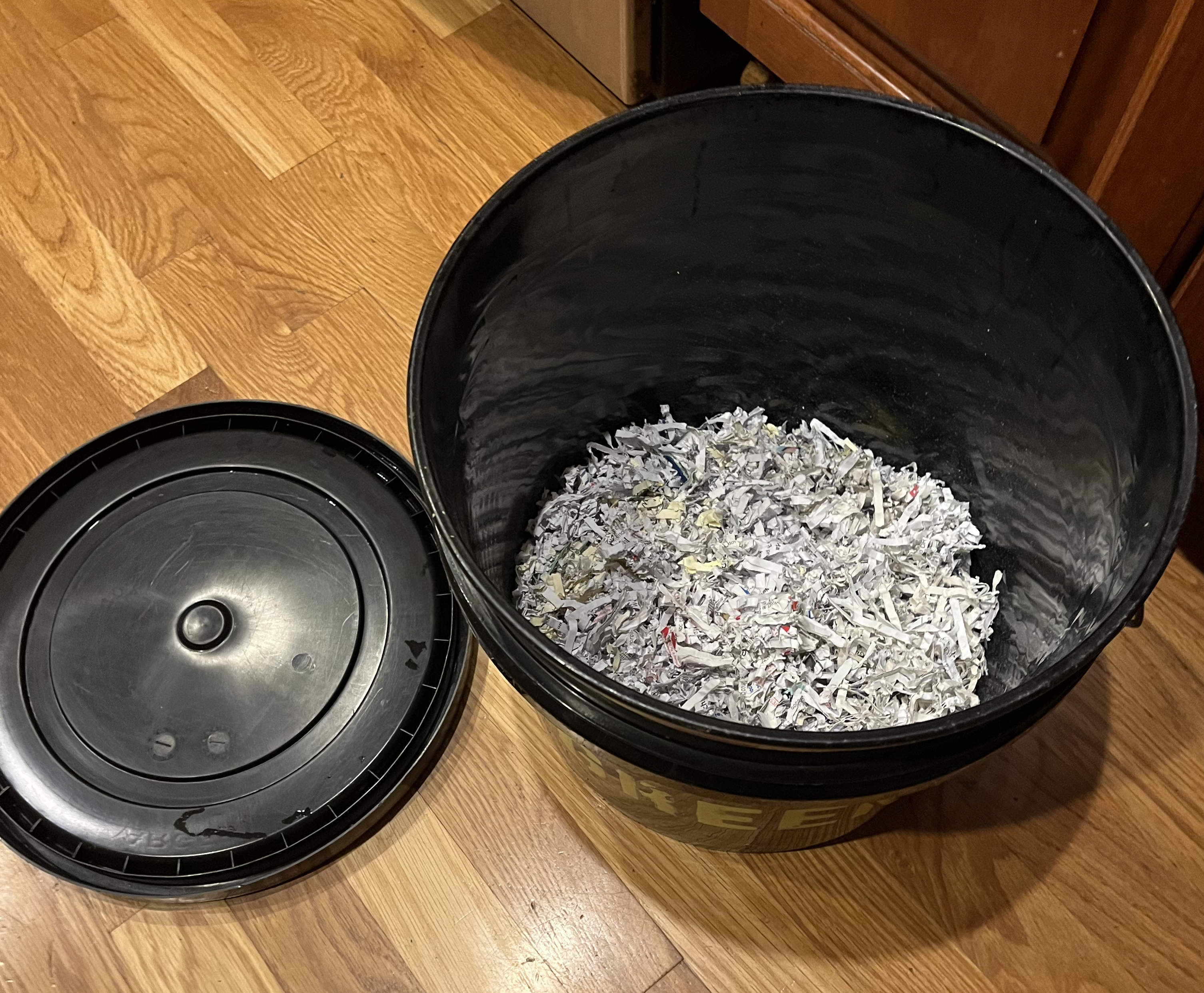 Photo of open black bucket with shredded paper inside and black lid beside it